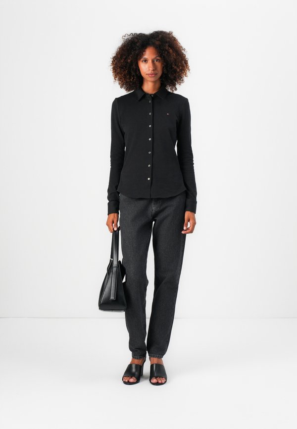Black long-sleeved button-up shirt with a collar, teamed with dark grey jeans, black slide sandals, and a black handbag. Simple design.