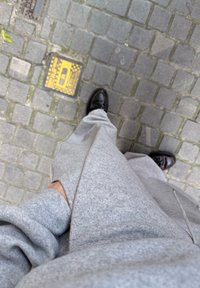 Personne en pantalon de survêtement gris et chaussures noires debout sur un pavé en pierres à côté d'une petite trappe utilitaire jaune.