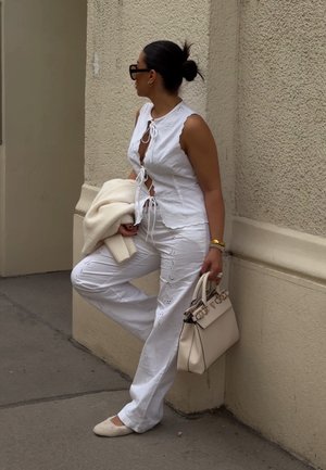 Balta, nėrinių apvadu papuošta, be rankovių palaidinė derinama su plačiomis kelnėmis, kurių audinyje yra skylučių raštų. Laikoma šviesiai ruda, minkšto tekstūros rankinė.