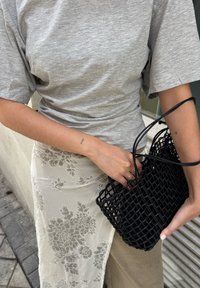 Camisa gris de manga corta, falda de encaje floral en beige claro y un pequeño bolso negro trenzado con asas delgadas.