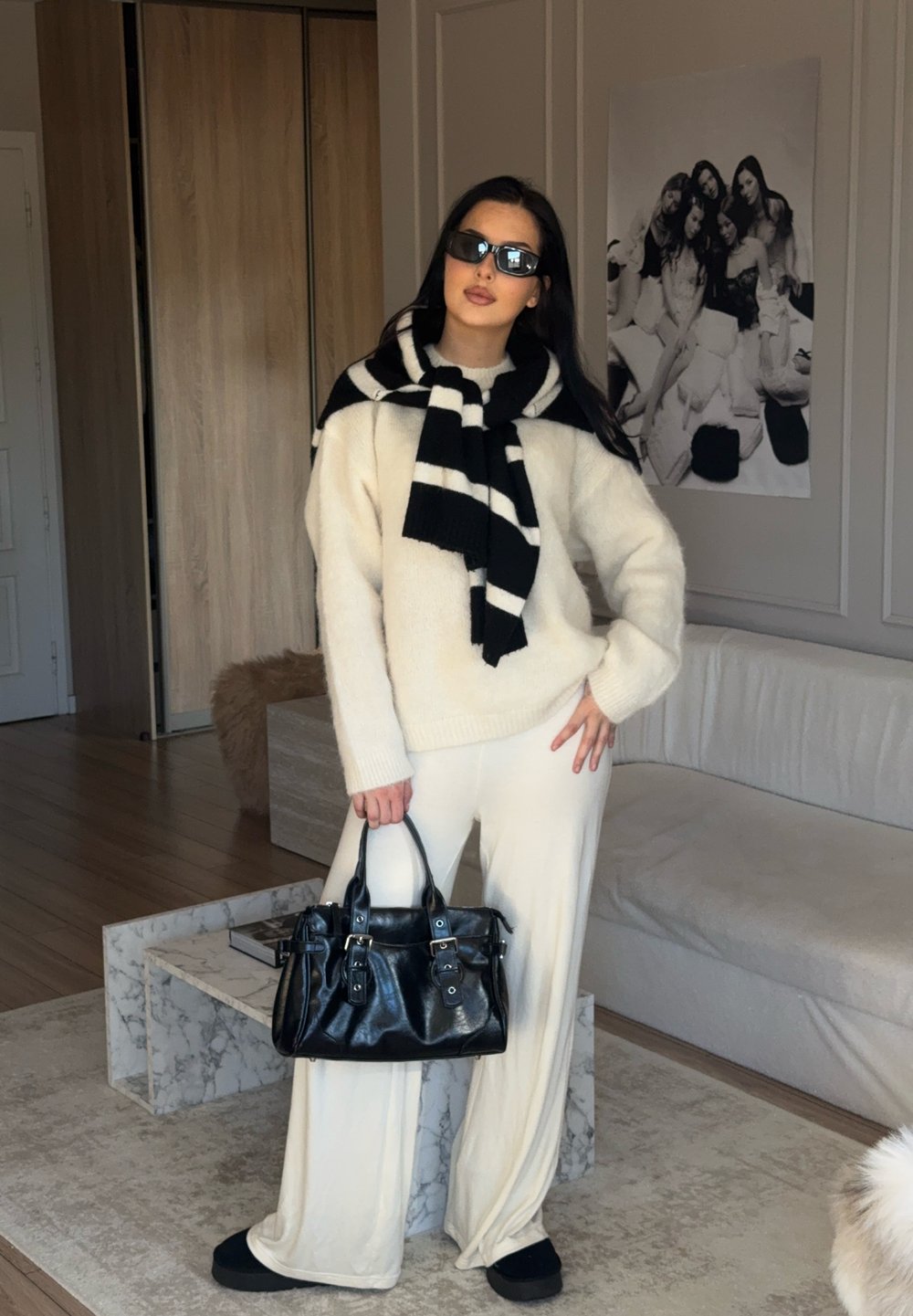 Oversized cream jumper, wide white trousers, black and white striped scarf, and a black leather handbag with metal accents. Black sunglasses.