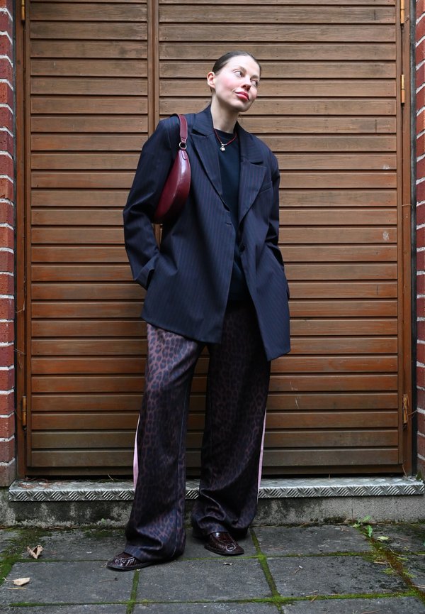 Overmaatse zwarte pinstripe blazer over een zwarte top, gecombineerd met bruine panterprint broek. Gecombineerd met een bordeauxkleurige tas en donkere schoenen.