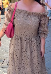 Καφέ φόρεμα με ανοιχτούς ώμους, με υφασμάτινο σχέδιο με κυψέλες και φουσκωτά μανίκια, συνδυασμένο με μία φωτεινή ροζ τσάντα.