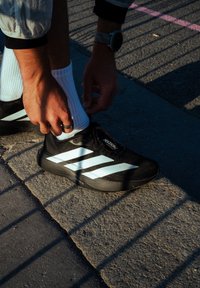 Čierne atletické topánky s bielymi pruhmi, ľahká konštrukcia, texturovaný zvršok, šnurované, nosené s bielymi ponožkami, na pozadí betónu.