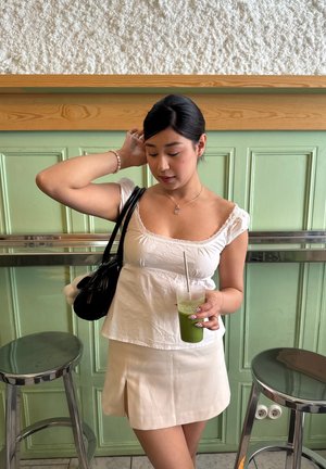 Top blanco de manga corta con encaje, falda mini beige con abertura lateral, sosteniendo un vaso transparente con bebida verde, bolso negro, diseño de decoración de uñas.