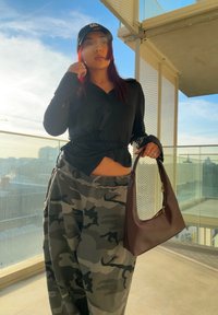 Black button-up top, grey camo sweatpants with an elastic waistband, and a brown leather bag with gold hardware. The background features a cityscape.