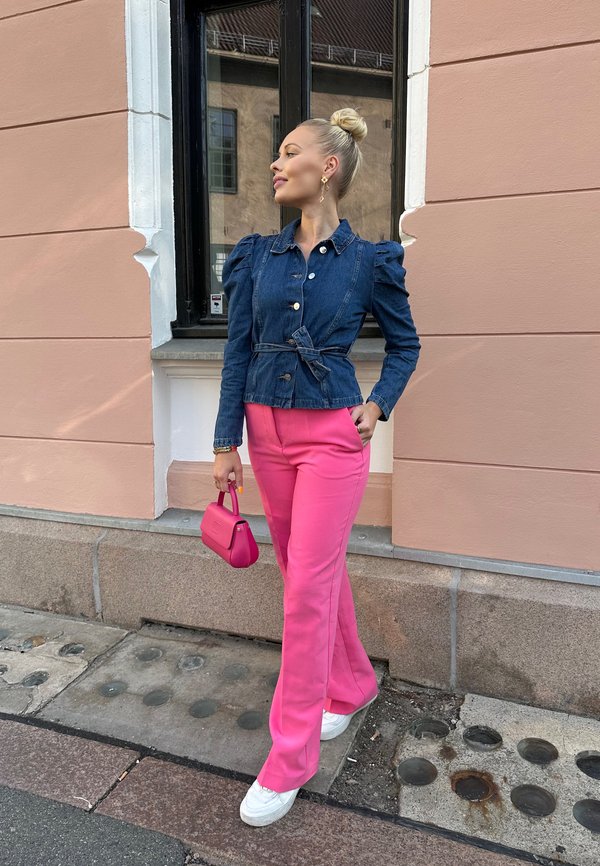 Veste en denim avec des manches bouffantes, taille ceinturée, couleur bleue ; pantalon rose évasé ; baskets blanches ; petit sac à main rose.