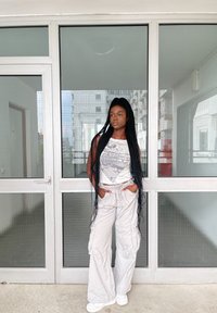 Μοντέλο φορώντας μια λευκή μπλούζα με γραφικά και ανοιχτό γκρι cargo παντελόνι, με χαλαρή εφαρμογή και τσέπες. Το φόντο περιλαμβάνει γυάλινες πόρτες και ένα σύγχρονο κτίριο.