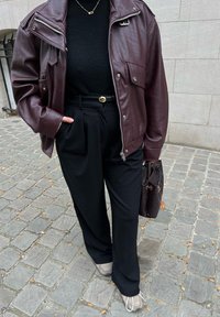 Veste oversize en cuir bordeaux, col roulé noir, pantalon noir sur mesure avec ceinture dorée, chaussures grises et sac à main noir tissé.