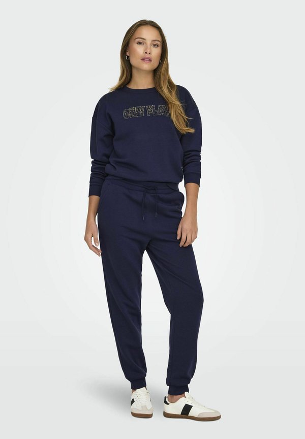 Donkerblauwe sweatshirt en joggers set, met een textuur graphic op de voorkant, ribgebreide boorden en een trekkoord in de taille, gecombineerd met witte sneakers.