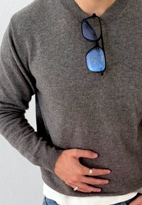 Grå strikket sweater med rund hals, der har ribbede manchetter. Sorte solbriller hviler på halsen. Laget hvid undertrøje er synlig ved sømmen.