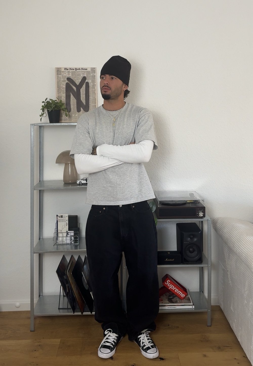 Hallide hallaste varrukatega t-särk, mis on valge pika varrukaga särgi peal, vabad mustad püksid, must beanie ja mustade ja valgete jooksujalatsitega. Hõbedane kett. 