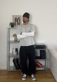 Hallide hallaste varrukatega t-särk, mis on valge pika varrukaga särgi peal, vabad mustad püksid, must beanie ja mustade ja valgete jooksujalatsitega. Hõbedane kett. 