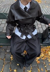 Fekete bőr, dupla soros zakó nagy gallérral, világoskék inggel és laza sötét nadrággal párosítva, egy padon ülve.