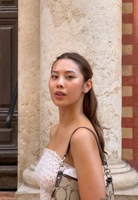 Strapless vit klänning med ett rött mönster; axellångt hår; grå mönstrad handväska med silverdetaljer; texturerad stenbakgrund.