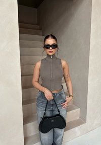 Tæt ribbet grå zip-up top parret med højtaljede lyseblå jeans og en sort buet håndtaske, sat mod en lys væg.