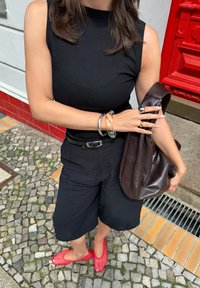 Svart ribbad ärmlös topp, vida svarta shorts, röda meshsandaler, silver- och guldsmycken, samt en brun läderaxelväska.