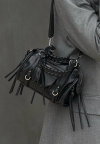Schwarze Lederhandtasche mit geflochtenem Henkel, Fransen-Details und silbernem Zubehör. Kompaktes Design mit Reißverschluss und seitlichen Taschen.