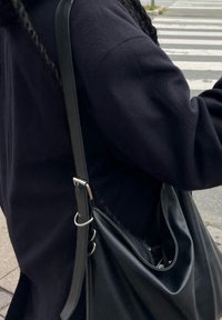 Fekete bőr kézitáska egyszálú pánttal, ezüst hardware részletekkel, sötét szövetből készült ruházaton viselve. Látható textúra és forma részletek.