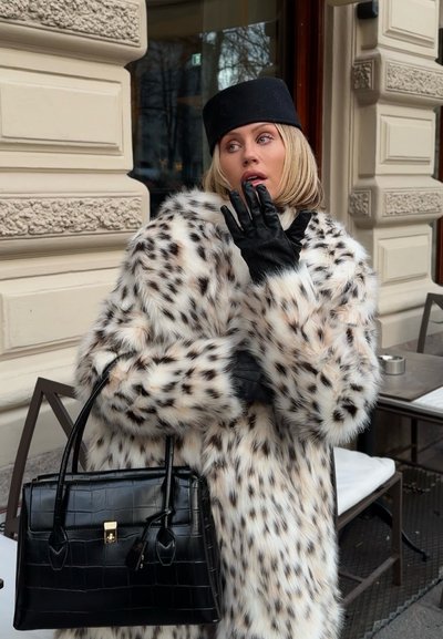 Abrigo blanco de piel sintética con manchas de leopardo, guantes de cuero negro y un bolso negro texturizado. El abrigo presenta un diseño voluminoso y un cuello ancho.