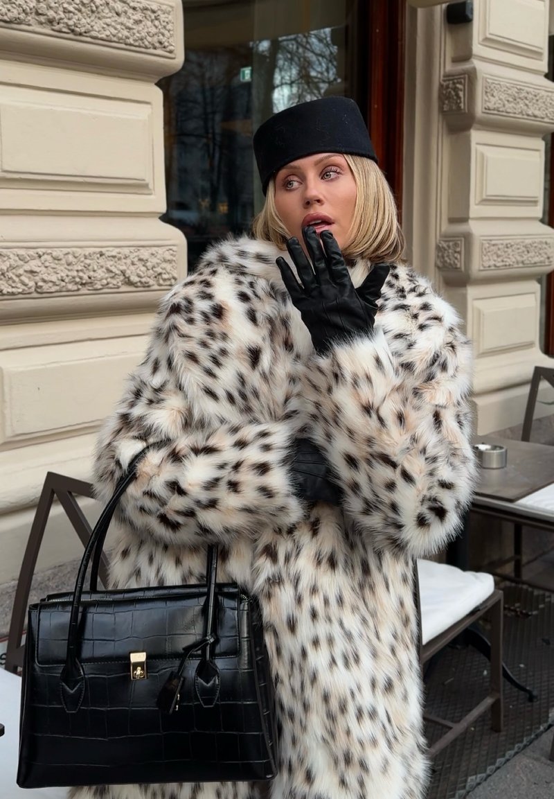Weißer Kunstpelzmantel mit Leopardenflecken, schwarze Lederhandschuhe und eine strukturierte schwarze Handtasche. Der Mantel hat ein voluminöses Design und einen breiten Kragen.