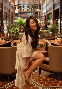 Robe en soie avec des manches larges, une fente haute et une finition texturée. Chaussure à talon dorée en train d'être levée. Intérieur élégant avec des plantes vertes.