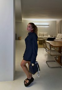 Jeanshemdkleid mit langen Ärmeln, dunkler Waschung, Knopfverschluss, kombiniert mit schwarzen Plateausandalen und einer strukturierten schwarzen Handtasche mit Ripsbandakzent.