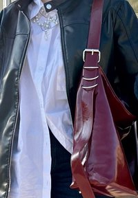 Schwarze Lederjacke mit silbernem Reißverschluss, weißes Hemd mit Knöpfen, und eine glänzende burgunderfarbene Handtasche mit verstellbarem Riemen und metallischen Akzenten.