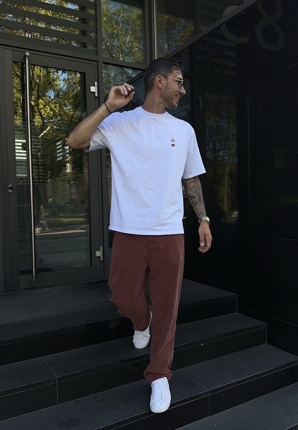 Hombre con gafas de sol, camiseta blanca y pantalones marrones bajando unas escaleras negras frente a la entrada de un edificio de vidrio.