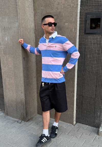 Polo de manga larga a rayas en azul y rosa con un cuello blanco, combinado con pantalones cortos negros y zapatillas negras con rayas blancas.