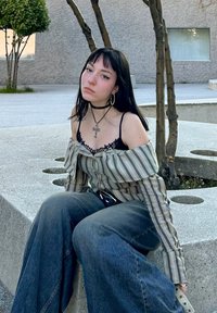 Ριγέ off-the-shoulder μπλούζα με φρουφρού άκρα, μαύρη δαντελένια υπομπλούζα, φαρδιές μπλε τζιν παντελόνες, και ασημένια σκουλαρίκια κρίκοι με κρεμαστό σταυρό.