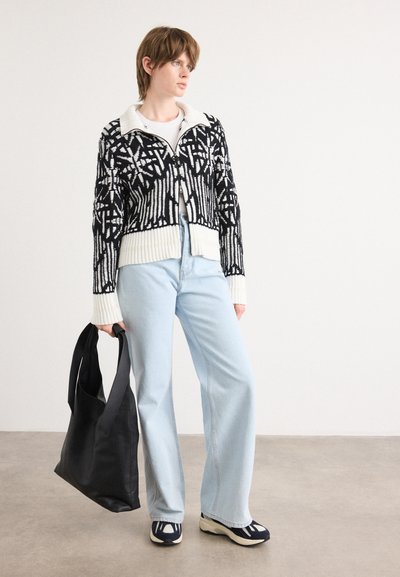 Cárdigan de patrón en blanco y negro con dobladillo acanalado, jeans de pierna ancha azul claro y un bolso negro de hombro. Los zapatos presentan un diseño en azul marino y blanco.