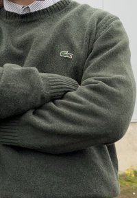 Zöld kötött pulóver bordázott mandzsettákkal, amelyen a mellkason egy kis hímzett krokodil logó található. Puha tapintású és laza szabású.