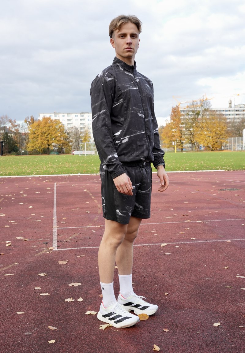 Completo sportivo composto da una giacca nera con motivi e pantaloncini abbinati, realizzati in tessuto leggero; abbinati a scarpe bianche con strisce nere.