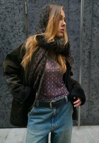 Καφέ υπερμεγέθης ζακέτα πάνω από ένα μοτίβο μωβ μπλουζάκι με μακριά μανίκια, συνδυασμένο με ψηλόμεσα τζιν. Σκούφο κασκόλ με λεοπαντί τυπώματα κρεμασμένο γύρω.