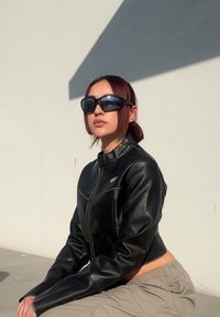 Czarna skórzana kurtka typu cropped z zamkiem z przodu, z wysokim kołnierzem i subtelnymi detalami szycia. Noszona z beżowymi spodniami dresowymi i okularami przeciwsłonecznymi.