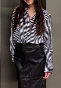 Chemise à boutons avec des rayures verticales bleu marine et blanches, associée à une jupe en cuir noir taille haute. Manches longues et coupe ajustée.