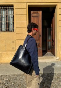 Czarna torba na ramię ze skóry o gładkiej fakturze, z dwoma solidnymi uchwytami. Projekt jest prosty i kanciasty, tworząc minimalistyczny wygląd.