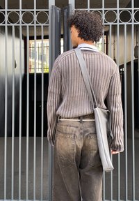 Grey ribbed sweater with long sleeves and a light grey shoulder bag, paired with high-waisted dark grey jeans, standing in front of a metal gate.