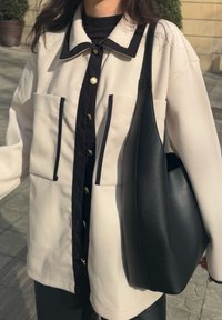 Κρέμ και μαύρο σακάκι με κουμπιά, με δύο μπροστινές τσέπες και χρυσά κουμπιά. Μαύρη δερμάτινη τσάντα ώμου με λεία επιφάνεια.