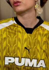 Geel Puma sportshirt met een textuurpatroon, zwarte kraag, witte accenten en een prominente witte logo aan de voorkant.