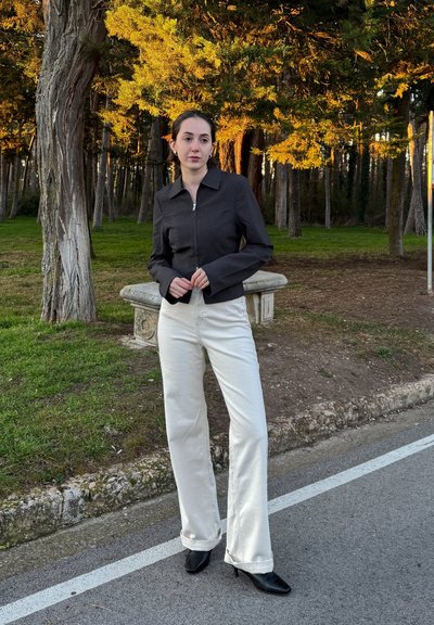 Chaqueta negra corta con cremallera frontal, combinada con pantalones blancos de pierna ancha y zapatos de tacón negros. Tejido suave y ajuste a medida.