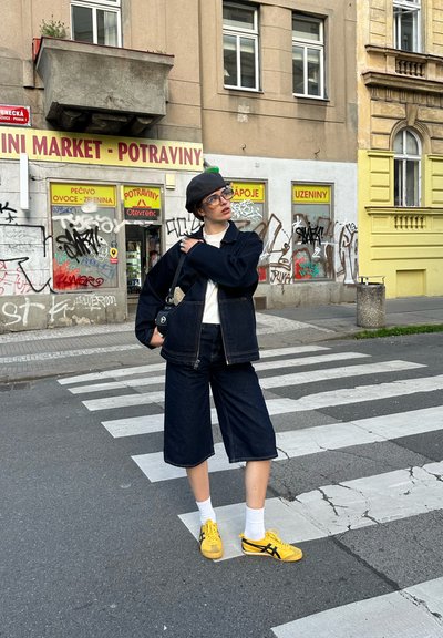 Chaqueta de mezclilla y pantalones cortos en azul oscuro, combinados con calcetines blancos y zapatillas amarillas con acentos negros, colocados en un paso de cebra.
