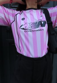 Rosa stripete sportsinnegen med en svart logo som leser "KØBENHAVN" med en teksturert aksent. Svart trim og ermer. Svart bukse brukt.