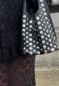 Čierna kožená taška s striebornými kopulovitými cvočkami, oblým tvarom a priestranným vnútrom; doplnená o čierny čipkovaný odev.