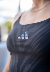 Top sportivo nero con un motivo testurizzato, caratterizzato da tre strisce verticali in un materiale lucido e scuro nell'area del petto.
