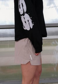 Shorts de sport beige clair à coupe ample, avec un petit logo blanc "SALOMON" sur le côté et une légère fente à l'ourlet.