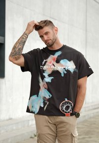Czarna koszulka z abstrakcyjnymi plamami niebieskiej i różowej farby, z napisem "HOOPTOPIA" oraz grafiką obręczy koszykarskiej na dolnej krawędzi.