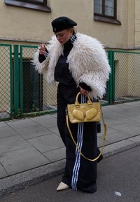 Black tracksuit with white stripes, fluffy white faux fur coat, black beret, yellow handbag with distinct accents, and beige pointed shoes.