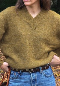 Sinise kollane V-kaelusega särk, millel on tekstureeritud kudumine, koos kõrge vöökohtadega denimplaadiga ja pruun nahkvööt, millel on metallist detailid.